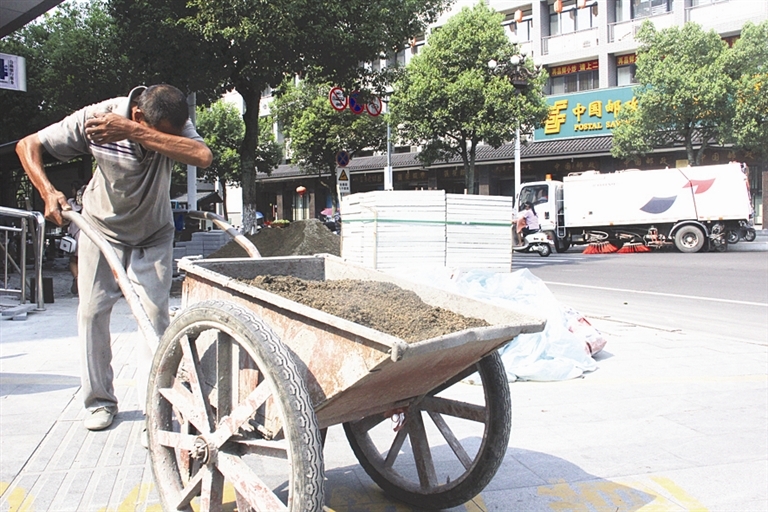 一名街道地面重铺工人,边推车,边擦汗