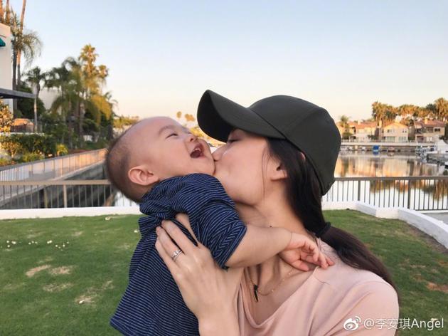 照片中李安琪把儿子抱在怀里,而淘气的宝宝伸手要摘妈妈头上的帽子