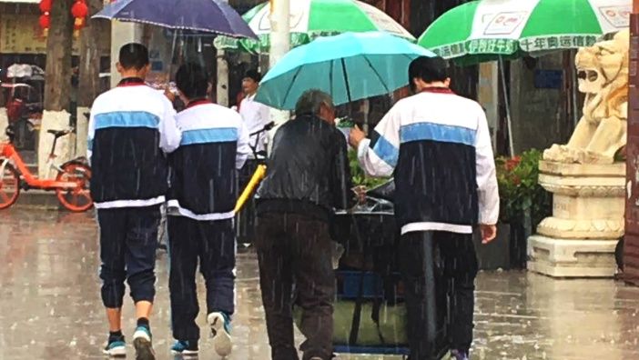 一名穿校服的男生,为推着老伴的大爷打伞,不顾自己淋雨的图片,刷爆