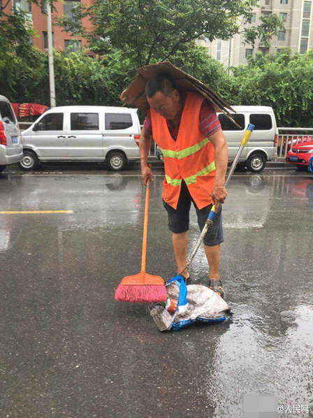 图为环卫工人头顶纸皮冒雨扫地.