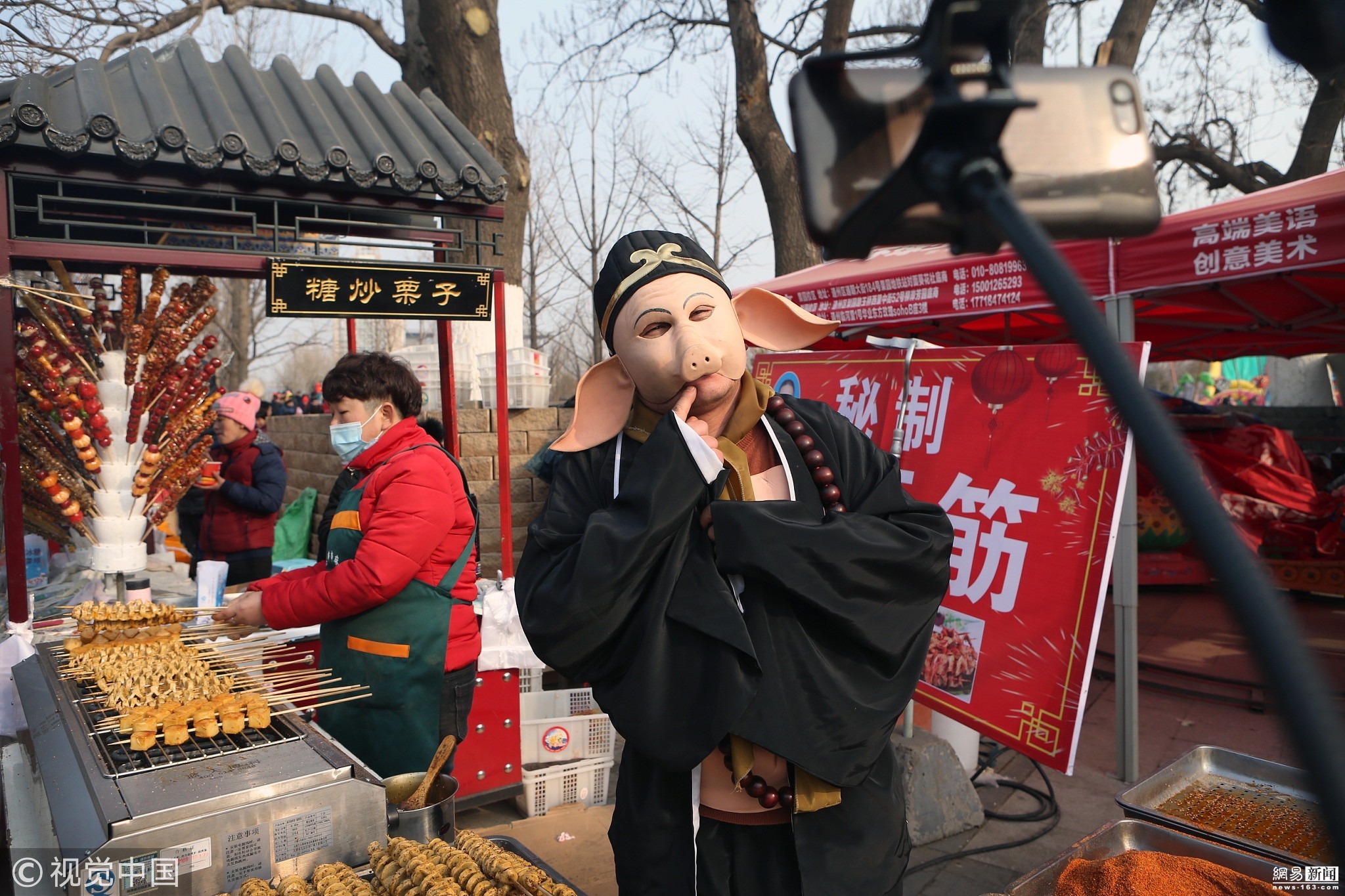 2019年2月6日下午，北京，在通州运河文化庙会上，一位小伙子头戴面具，装扮成猪八戒的形象，在动感音乐的伴奏下，跳着滑稽的舞蹈动作销售烤面筋，吸引了众人围观，人气好过周边的摊位。