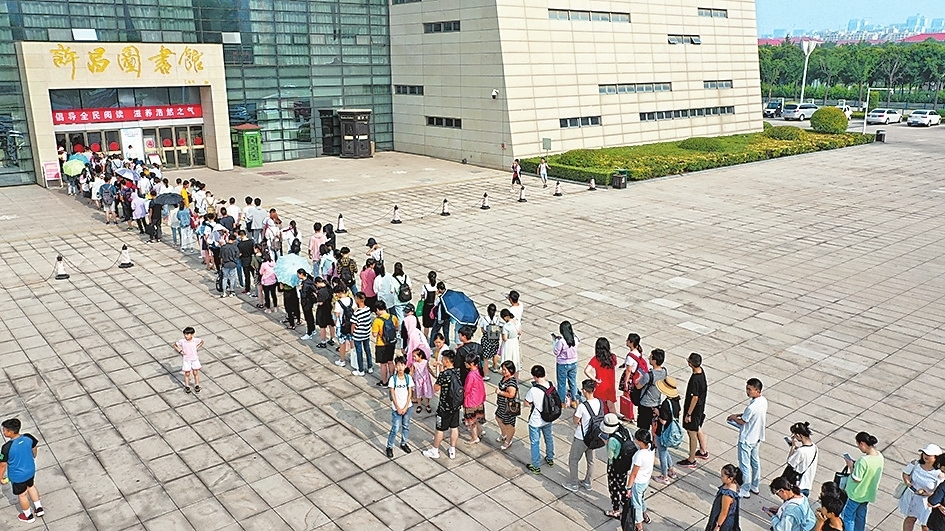 7月13日，市民在许昌图书馆门前排起长队等待进馆阅读。炎炎夏日，凉