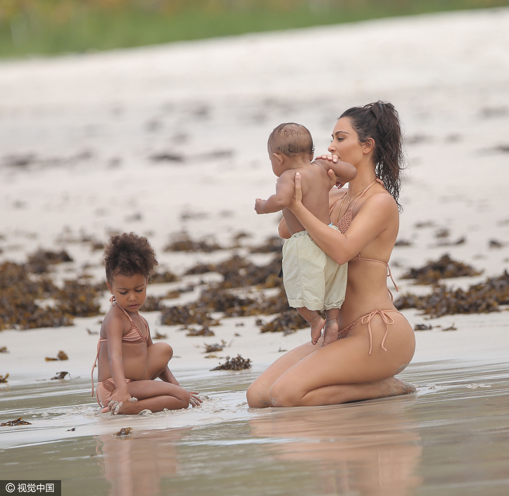 当地时间8月18日，金·卡戴珊（Kim Kardashian）带女儿小西北和儿子沙滩玩耍，卡戴珊身穿裸色系带比基尼，女儿与妈妈同款可爱十足，在沙滩上卡戴珊全程呵护幼子母爱爆棚，然而抢镜的还是翘臀。图为卡戴珊跪坐沙滩。