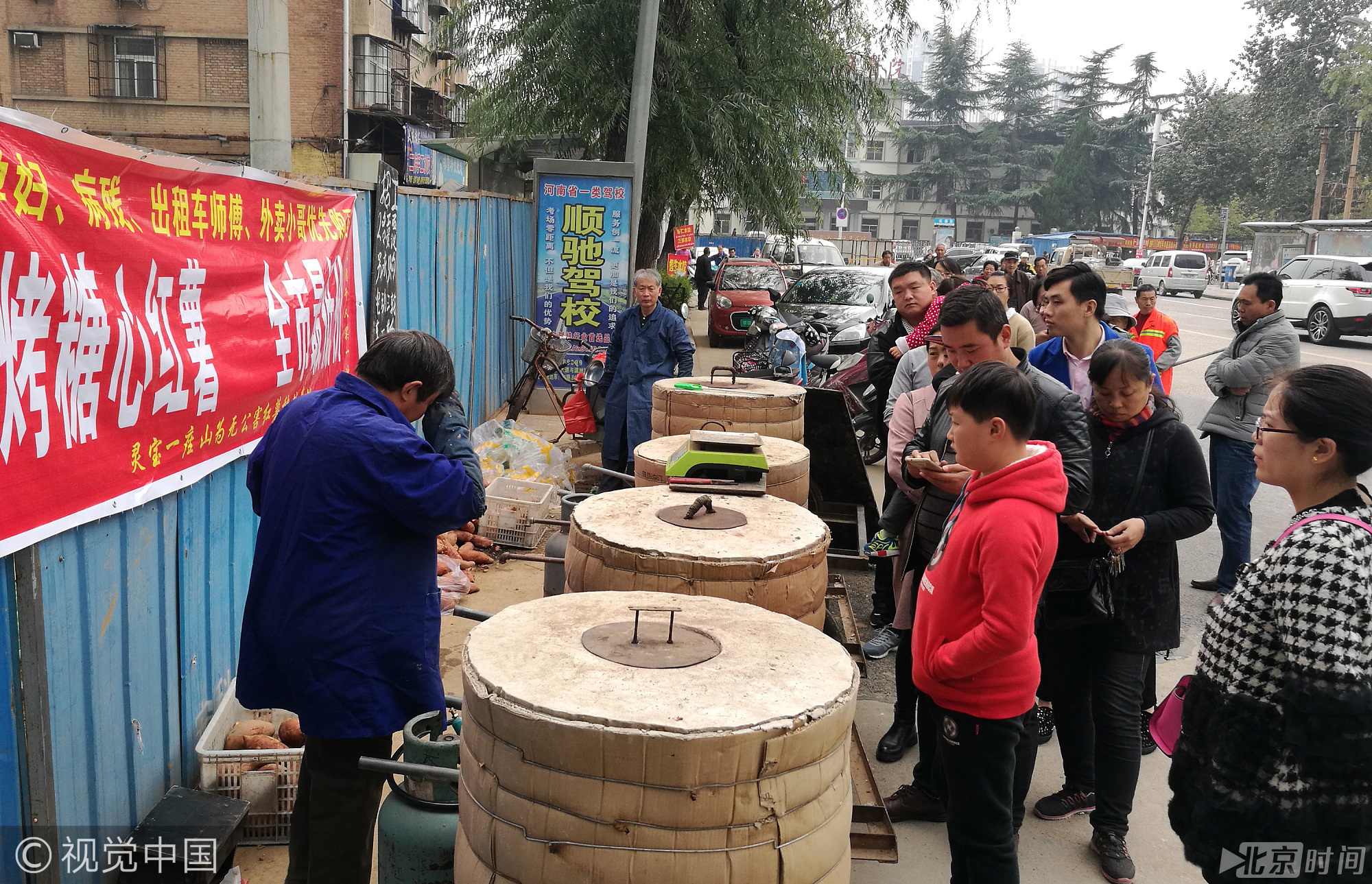 2017年10月21日，河南洛阳街头，一个卖烤红薯的摊位前架着4个大炉子，旁边排满了等待买烤红薯的市民。