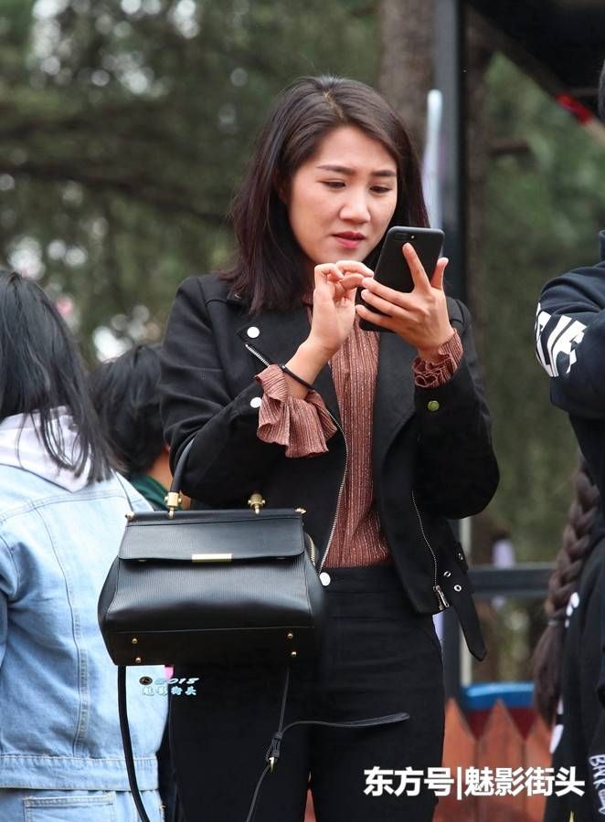 穿黑色牛仔衣、牛仔裤的美女,玩手机的样子非