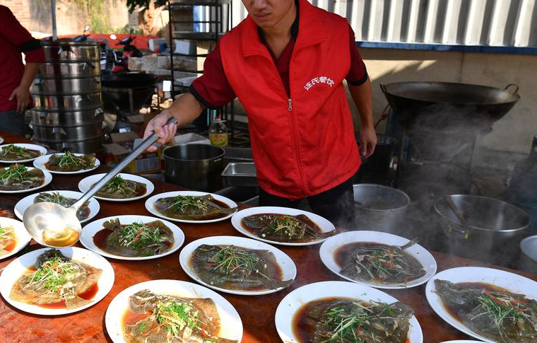 乡厨连辉腾称,虽然这次宴席的价格比较节俭,没有什么名贵的食材,但也可以达到中等水平。他做过的比较高档的宴席,一桌要三千到五千元。图为厨师往清蒸多宝鱼上浇热油。