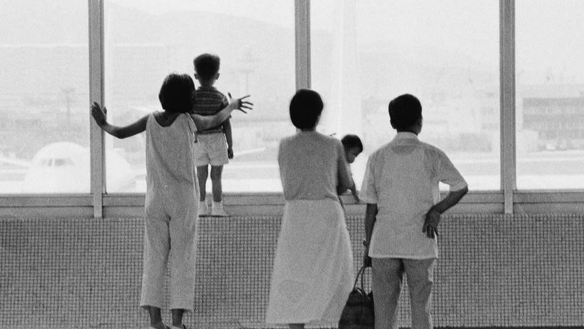 香港启德机场大堂，香港市民站在窗前张望，小朋友站在窗台上，妈妈在身后护着，很温馨。