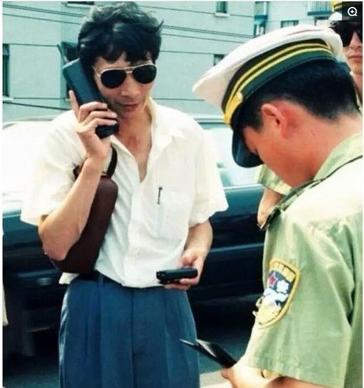 图为九十年代的一个“大款”，手上拿着大哥大和传呼机在接受警察的检查。
