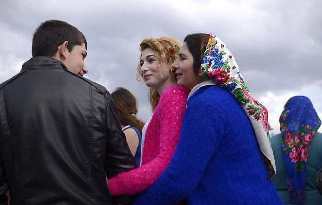 市场上随处可见三四十岁的中年人陪着孩子一起参加这场相亲盛会。图中的母亲从后面抱着女儿，打量着眼前的男子。